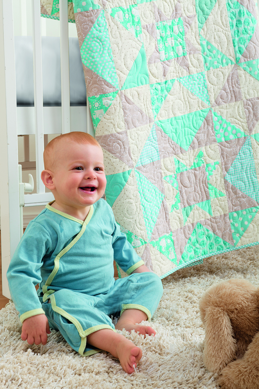 Free quilt pattern: Stardust Baby- cute baby sitting in front of the Stardust Baby quilt